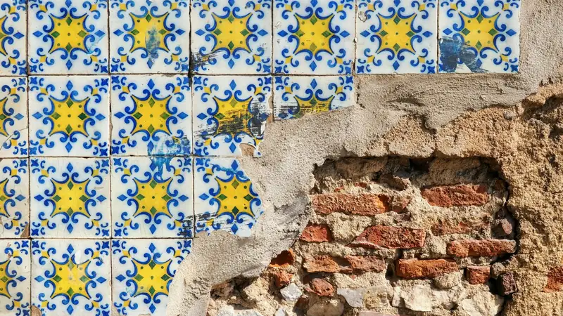 Carreaux anciens bleus et jaunes en partie tombés, laissant voir la brique