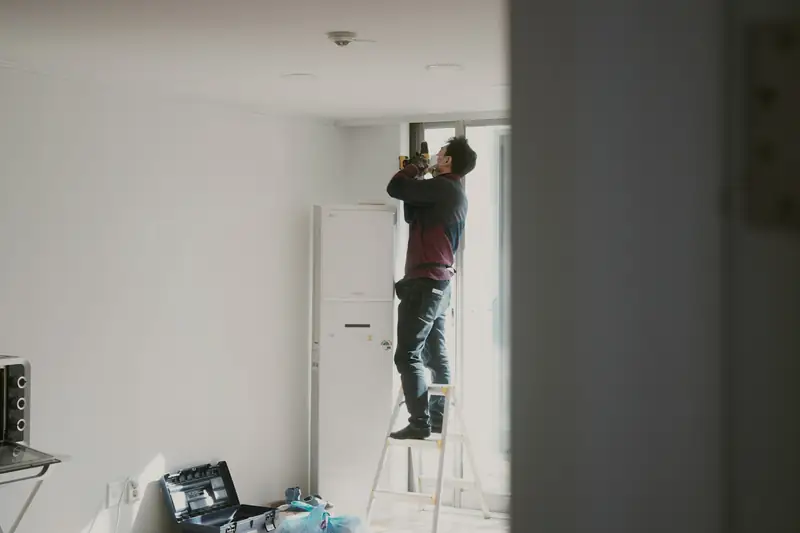 Ouvrier sur un escabeau qui travaille au plafond d’une pièce blanche