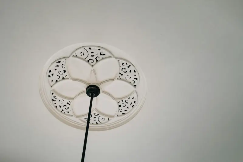 Rosace de plafond en plâtre ouvragé au centre d’un plafond blanc
